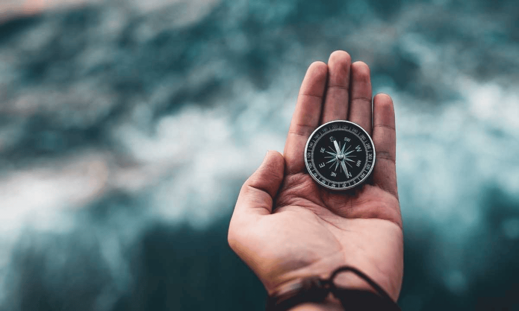 A hand holding a compass against a blurred background, symbolizing navigation and exploration.