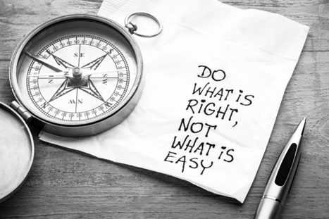 A compass beside a crumpled napkin with the phrase 'DO WHAT IS RIGHT, NOT WHAT IS EASY' written on it, on a wooden surface.